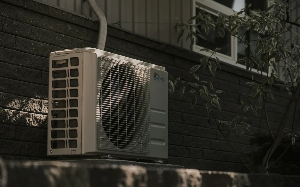 A ductless mini split outdoor unit mounted on a wall beside a window
